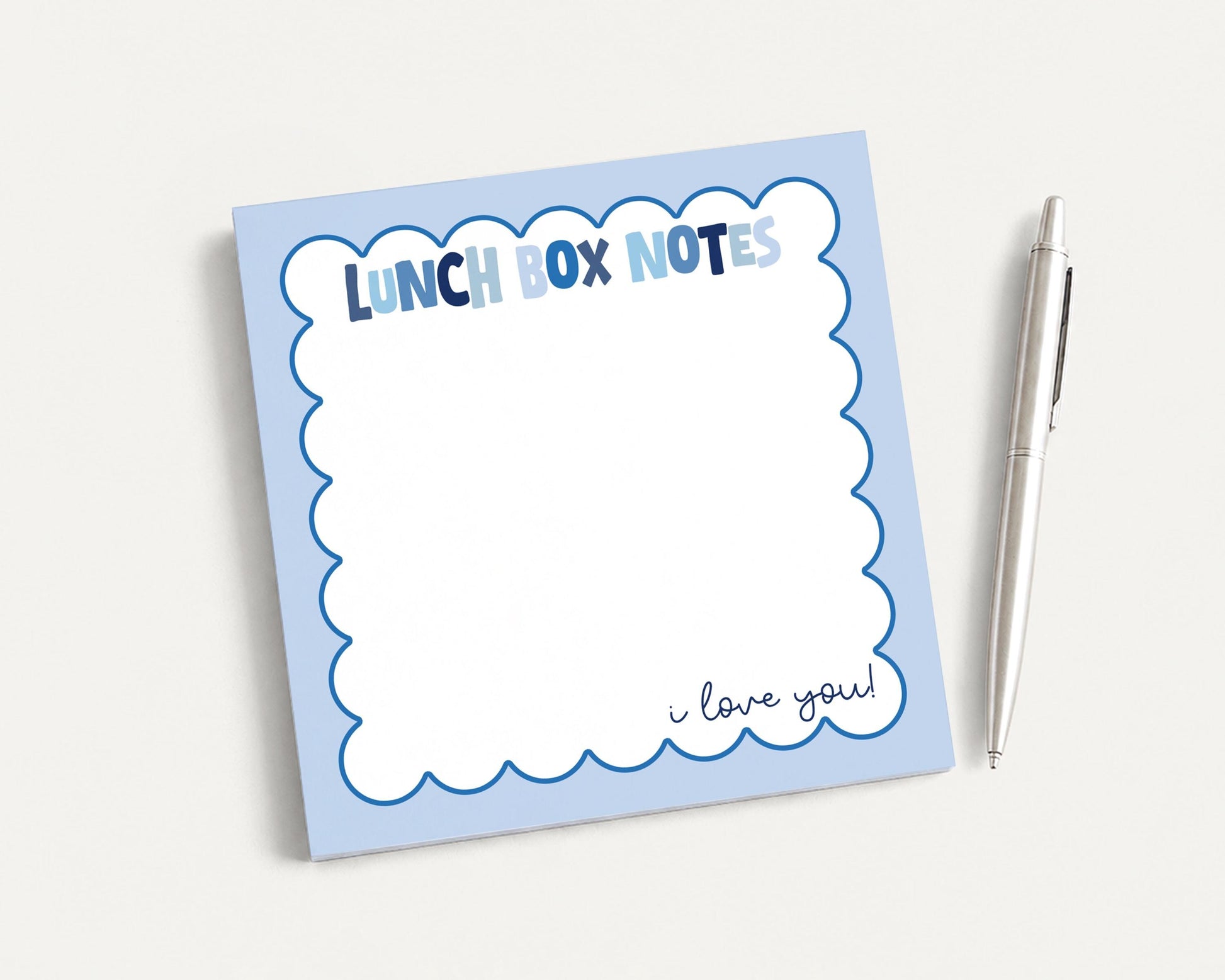 A blue and white lunch box note pad with a pen next to it.