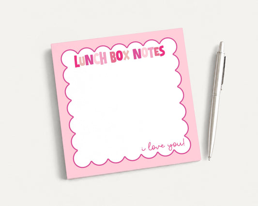 A pink sticky note pad with a blank space for writing and a pen next to it.