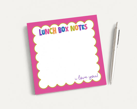 A pink sticky note pad with a blank space for writing and a pen next to it.