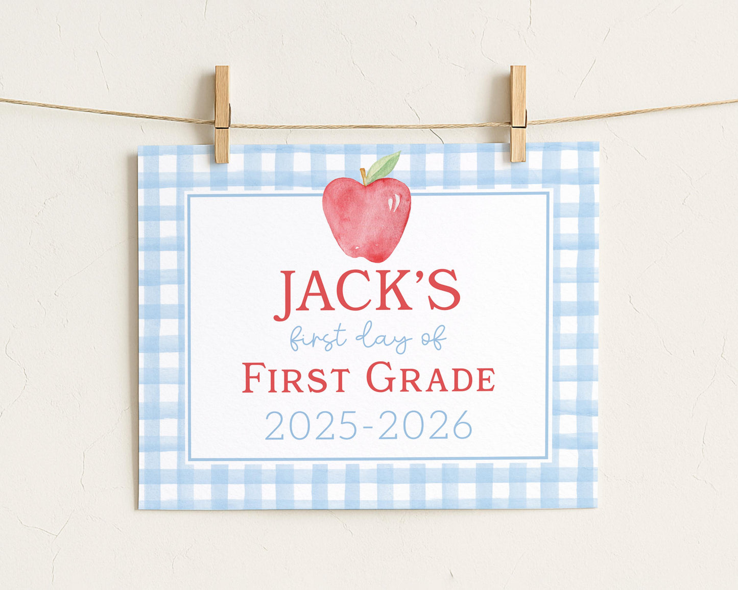 A blue and white checkered sign with a red apple and the text "JACK'S first day of FIRST GRADE" hanging on a clothesline.