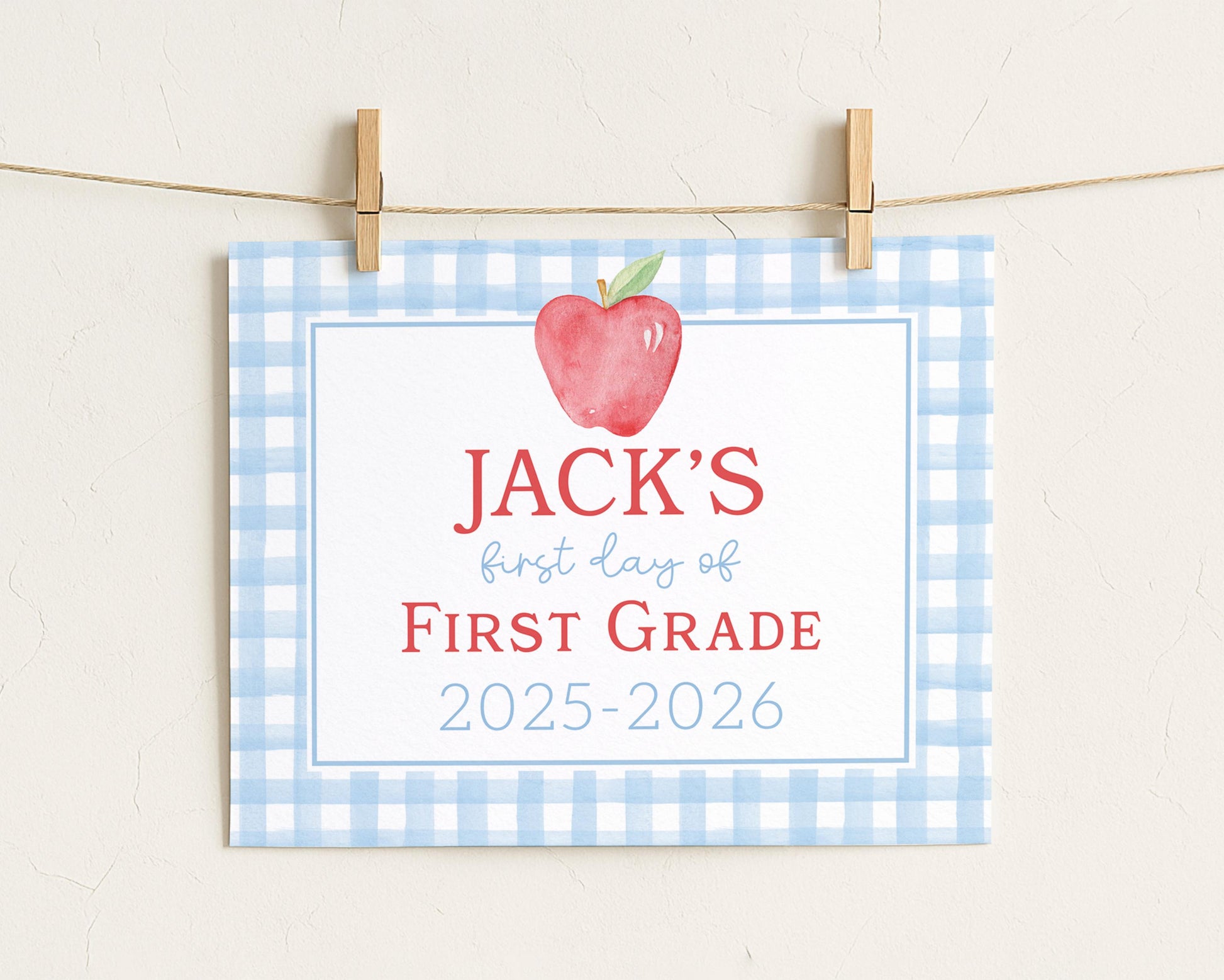 A blue and white checkered sign with a red apple and the text "JACK'S first day of FIRST GRADE" hanging on a clothesline.