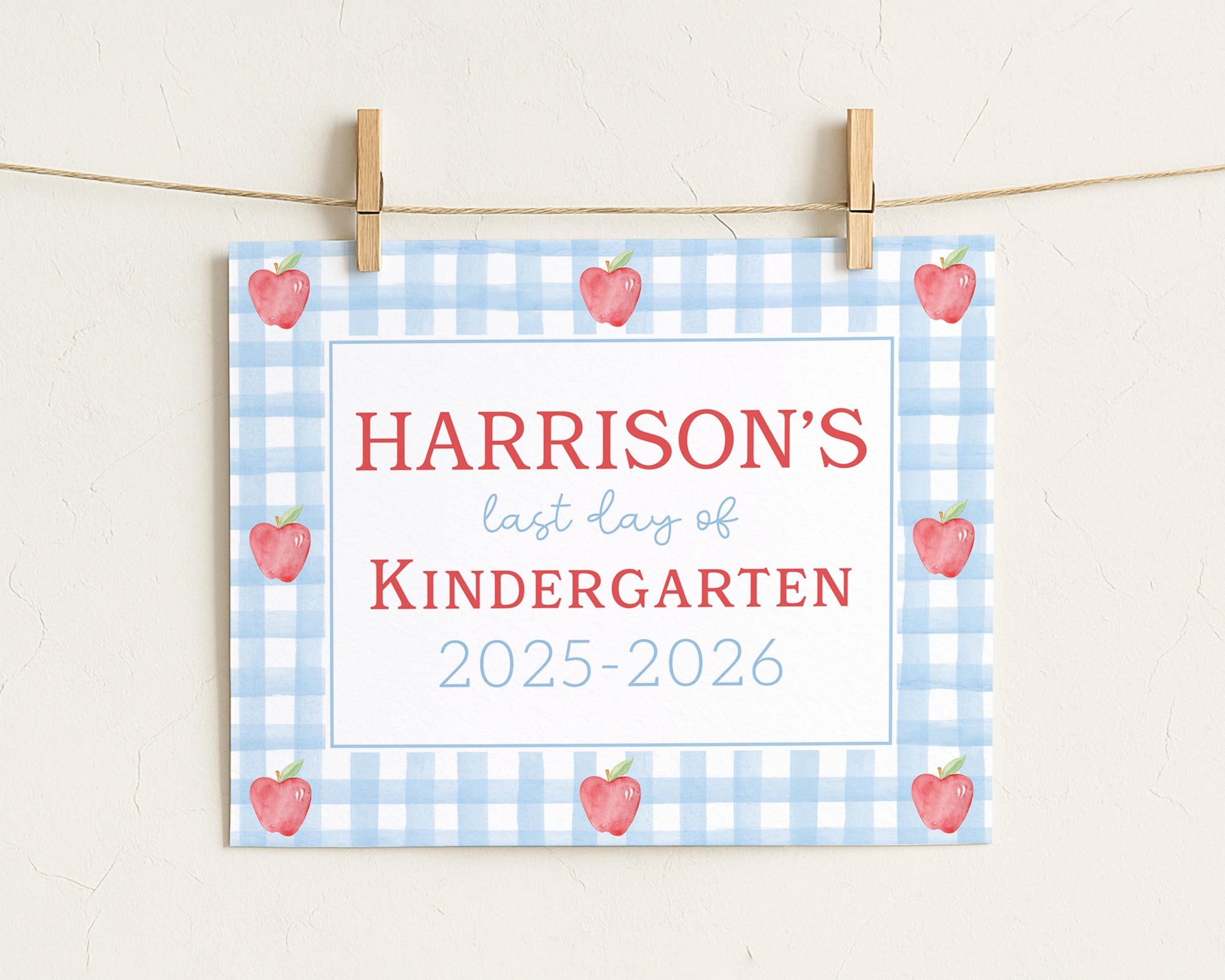 A sign with the text "HARRISON'S last day of KINDERGARTEN" and "2025-2026" printed on it, with a blue and white checkered background and red apples.