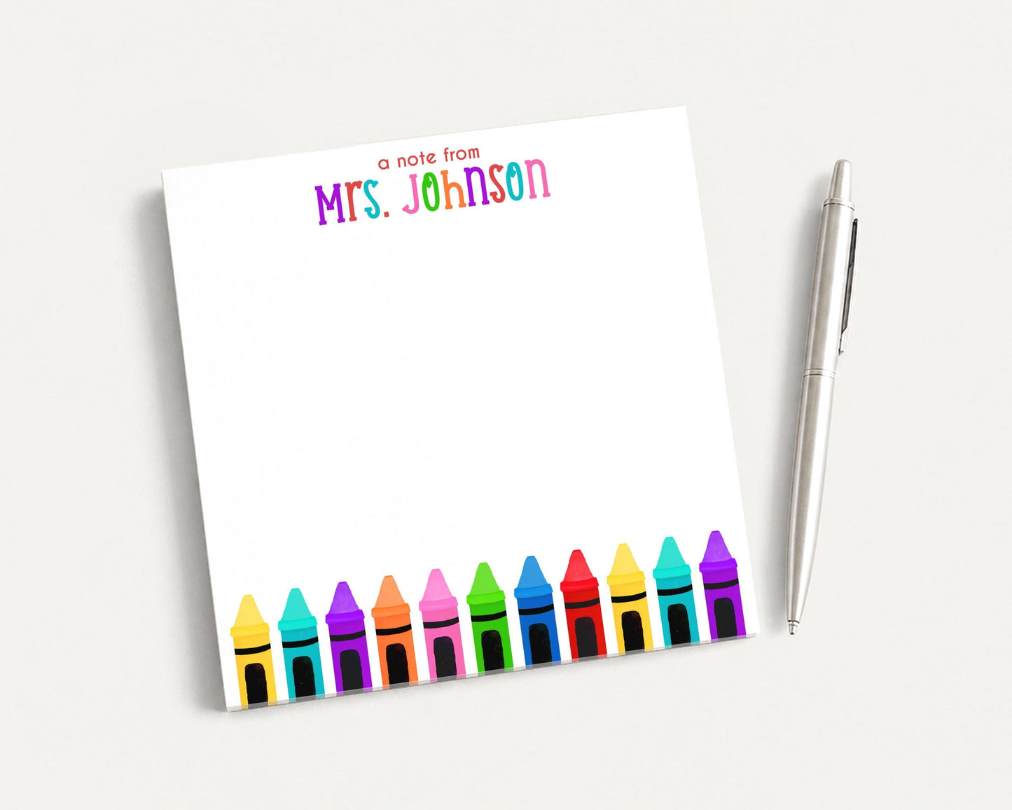 A blank white notepad with a colorful crayon border and a pen on a white surface.