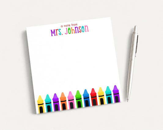 A blank white notepad with a colorful crayon border and a pen on a white surface.