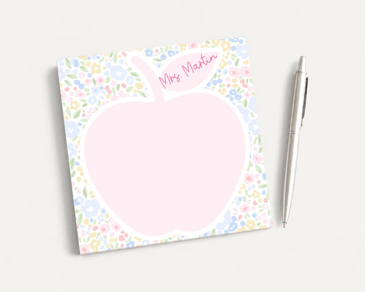 A pink flower-patterned notepad with a blank space in the center, accompanied by a silver pen on a plain white background.