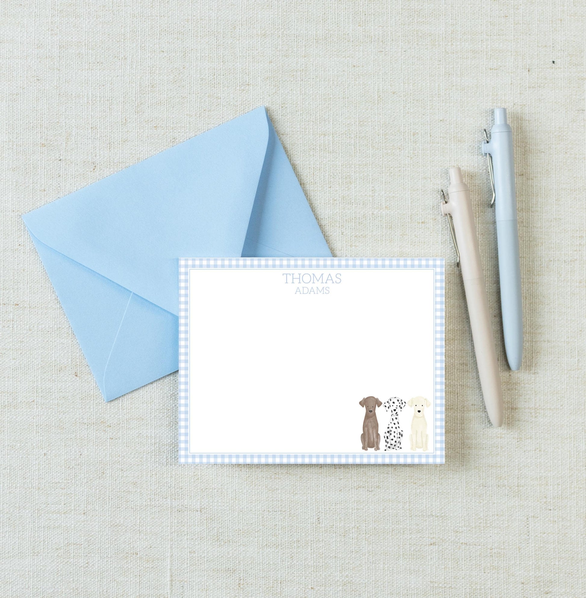 a blue envelope, a blank note card with a dog illustration, and three pens on a beige background.