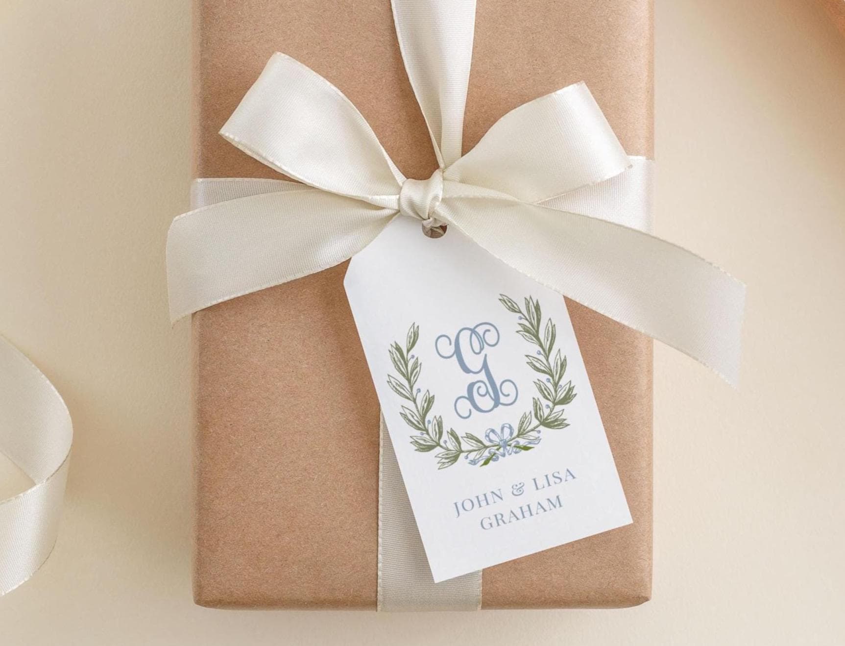 A brown gift box with a white ribbon and a monogrammed tag attached to it.