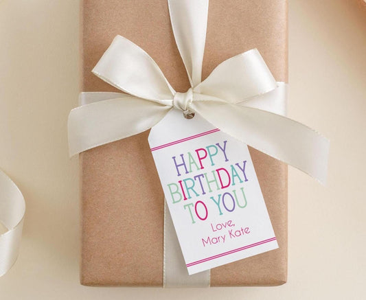 A brown gift box with a white ribbon and a white tag attached to it, which reads "Happy Birthday to You" and includes the names "Love, Mary Kate".