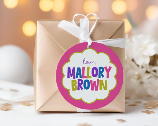 A gift box with a pink and white label that says "love, Mallory Brown" is placed on a table with white flowers in the background.