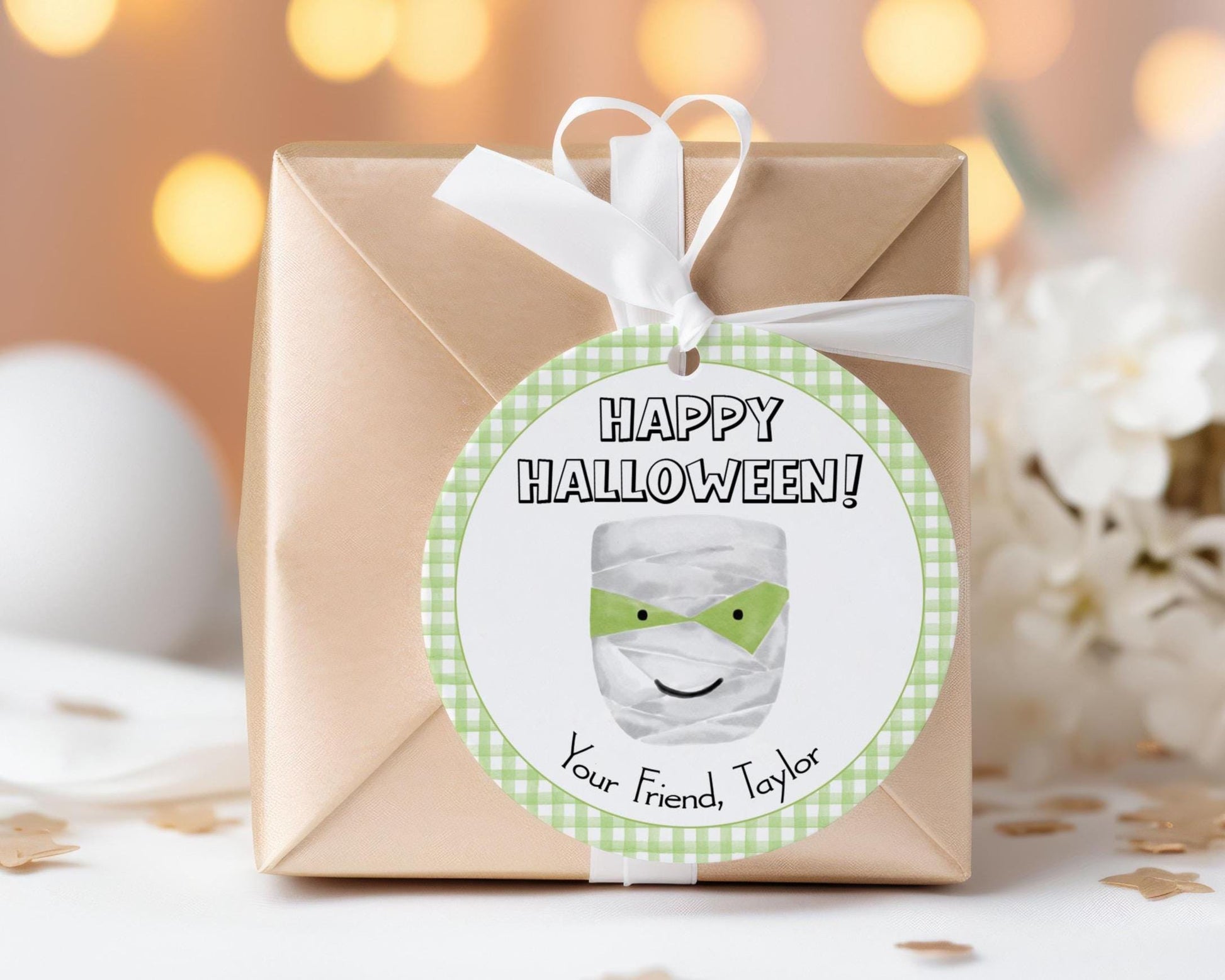 A brown gift box with a white ribbon and a round tag that reads "Happy Halloween!" and features a smiling face.