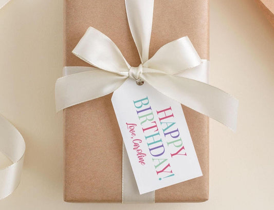 A brown gift box with a white ribbon and a personalized birthday tag attached to it.