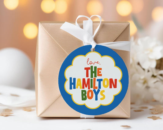 A gift box with a blue and white label that says "love, The Hamilton Boys" and a white ribbon tied around it.