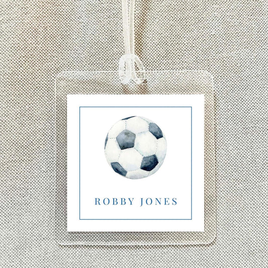 A clear plastic name tag with a soccer ball image and the name "ROBBY JONES" printed on it.