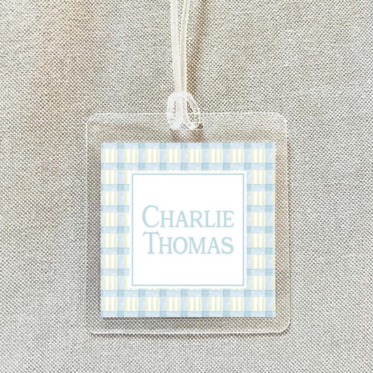 A clear plastic name tag with a blue and white checkered pattern and the name "Charlie Thomas" printed on it.