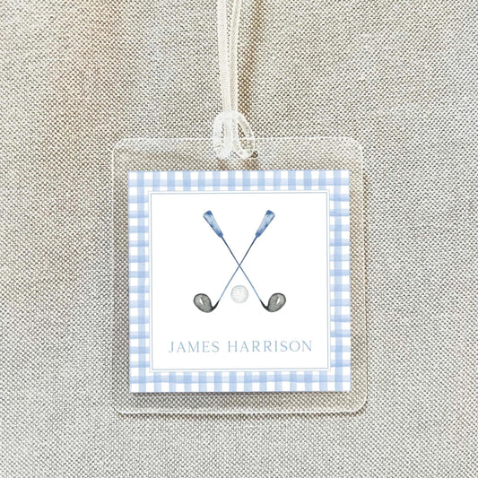 A clear plastic name tag with a blue and white checkered border, featuring a golf club and ball illustration, and the name "James Harrison" written below.
