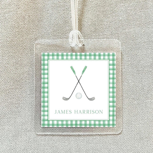 A clear plastic name tag with a green and white checkered border, featuring a golf club and ball graphic, and the name "James Harrison" written below.