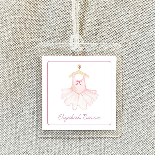 A clear plastic tag with a pink tutu and bow on it, hanging from a string.