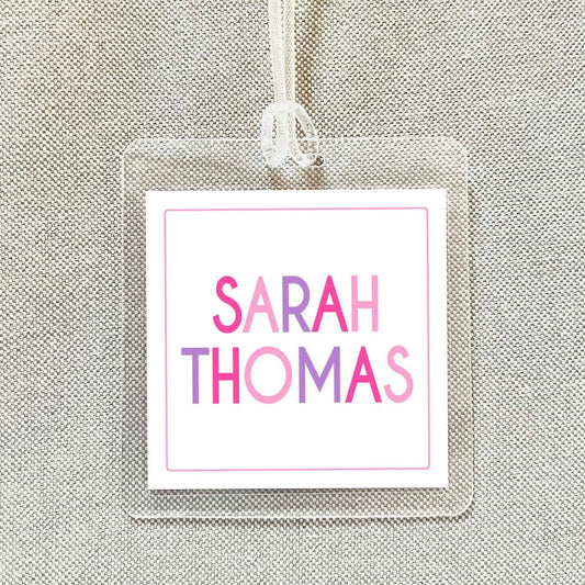 A clear plastic name tag with the name "SARAH THOMAS" printed on it in pink and purple colors.