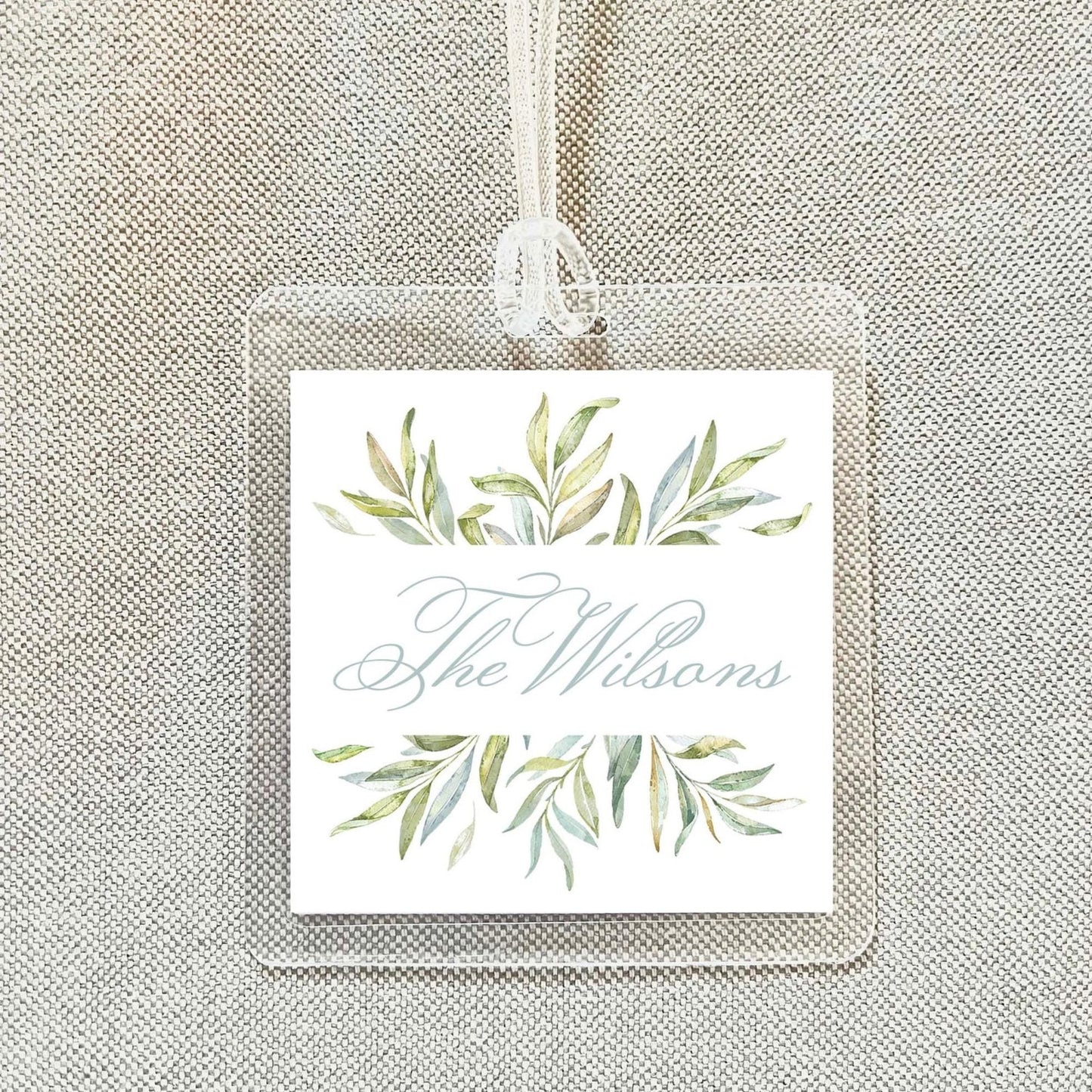 A square tag with a floral design and the name "The Wilsons" written on it, hanging on a string.