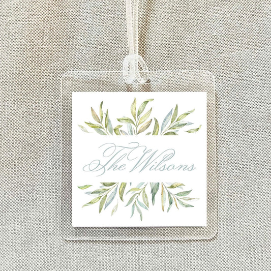 A square tag with a floral design and the name "The Wilsons" written on it, hanging on a string.