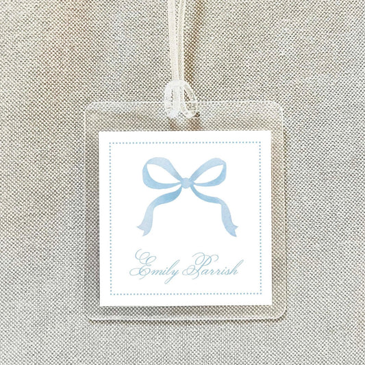 A clear plastic name tag with a blue ribbon design and the name "Emma Barrish" printed on it.