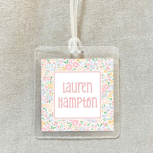 A clear plastic name tag with a floral design and the name "Lauren Hampton" printed on it.