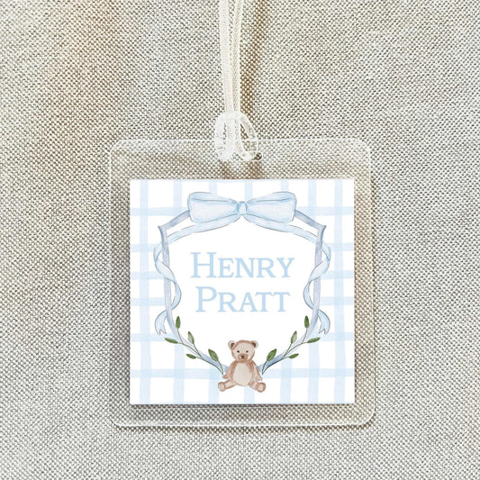 A clear plastic tag with a blue and white checkered background, featuring a teddy bear and a ribbon.