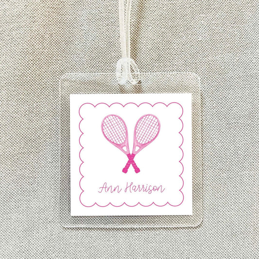 A clear plastic name tag with a pink tennis racket design and the name "Ann Harrison" written on it.