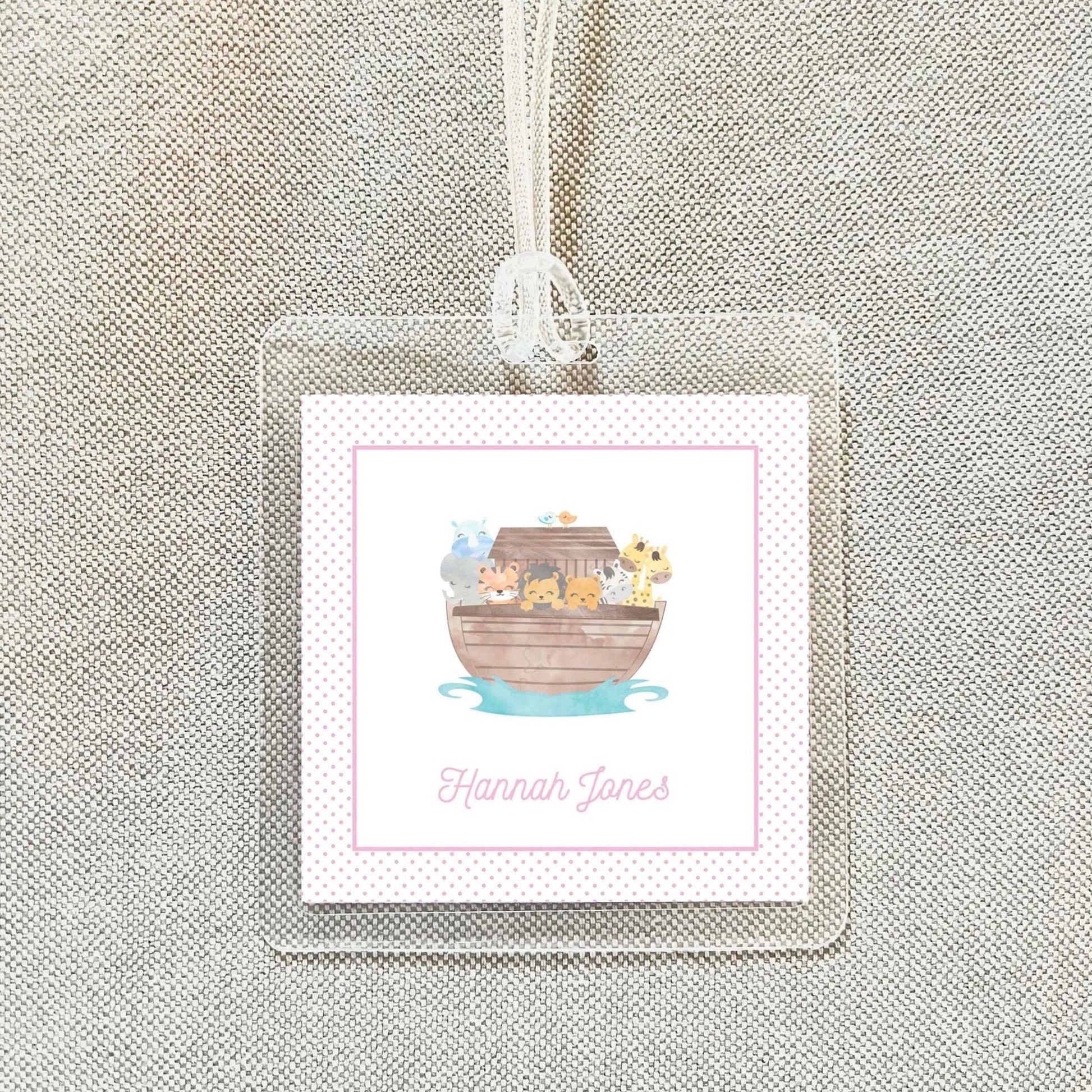 A clear plastic name tag with a pink border and a cartoon illustration of a boat filled with animals.