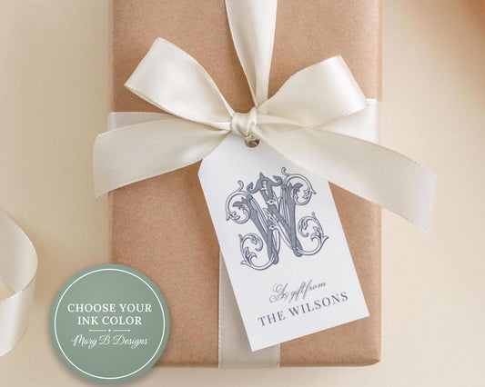 A brown gift box with a white ribbon and a monogrammed tag attached to it.
