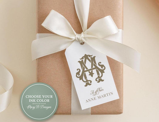 A brown gift box with a white ribbon and a monogrammed tag attached to it.