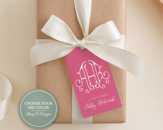A gift box wrapped in brown paper with a pink ribbon and a white tag displaying a monogram.