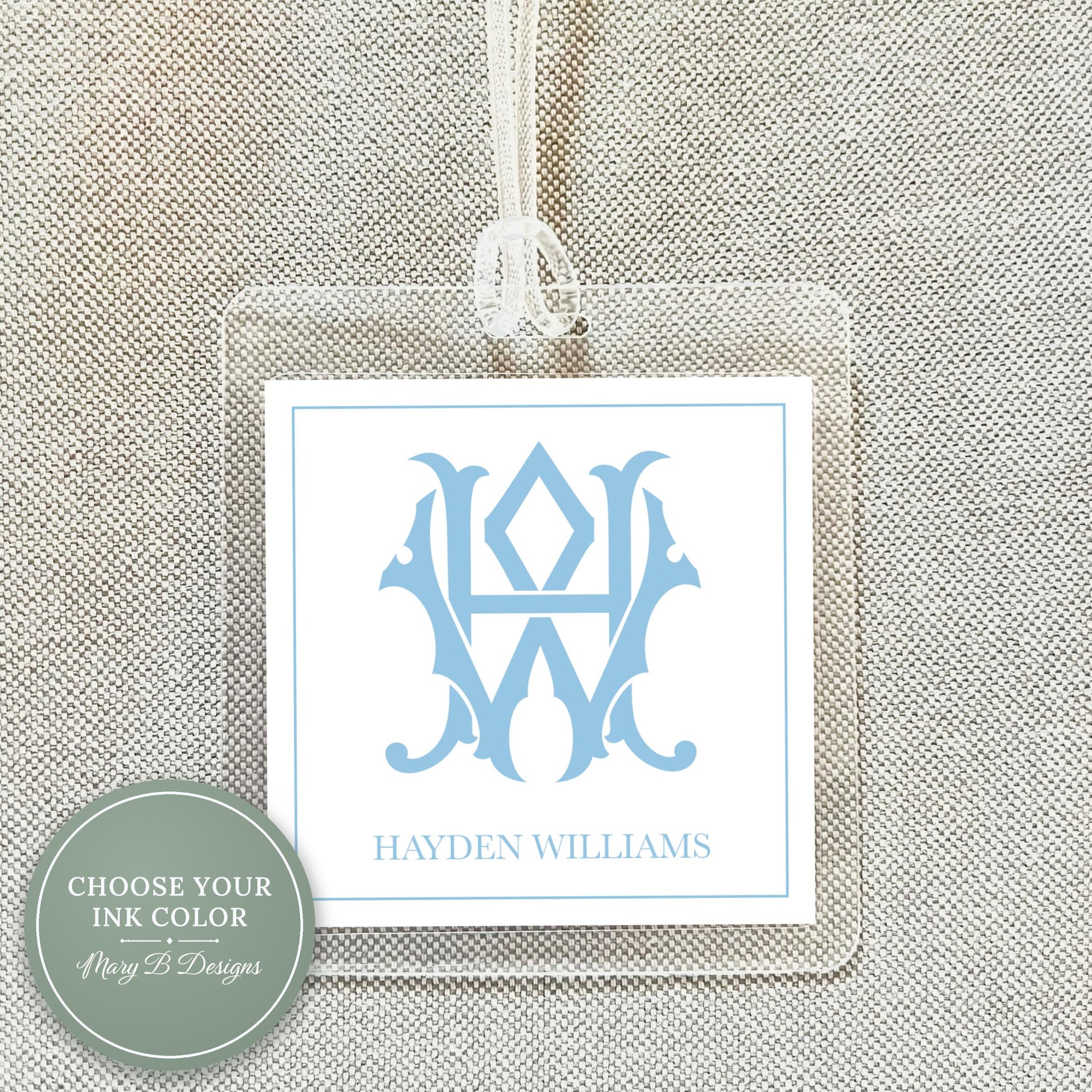 A clear plastic name tag with a monogrammed logo hanging from a string.