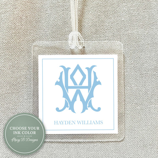 A clear plastic name tag with a monogrammed logo hanging from a string.