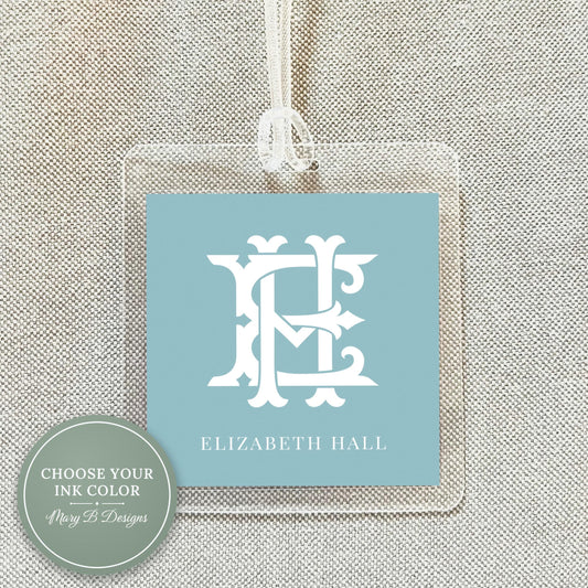 A clear plastic name tag with a monogrammed logo hanging from a string.