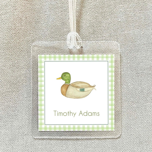 A clear name tag with a green and white checkered border, featuring a cartoon duck illustration.