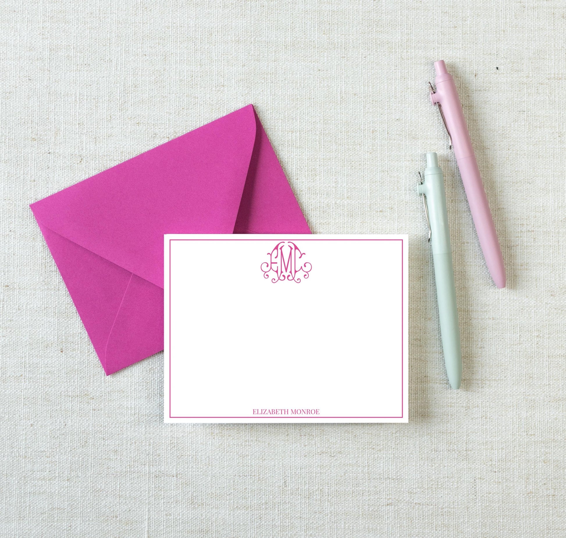 a pink envelope, a pink pen, and a light blue pen on a light beige background.
