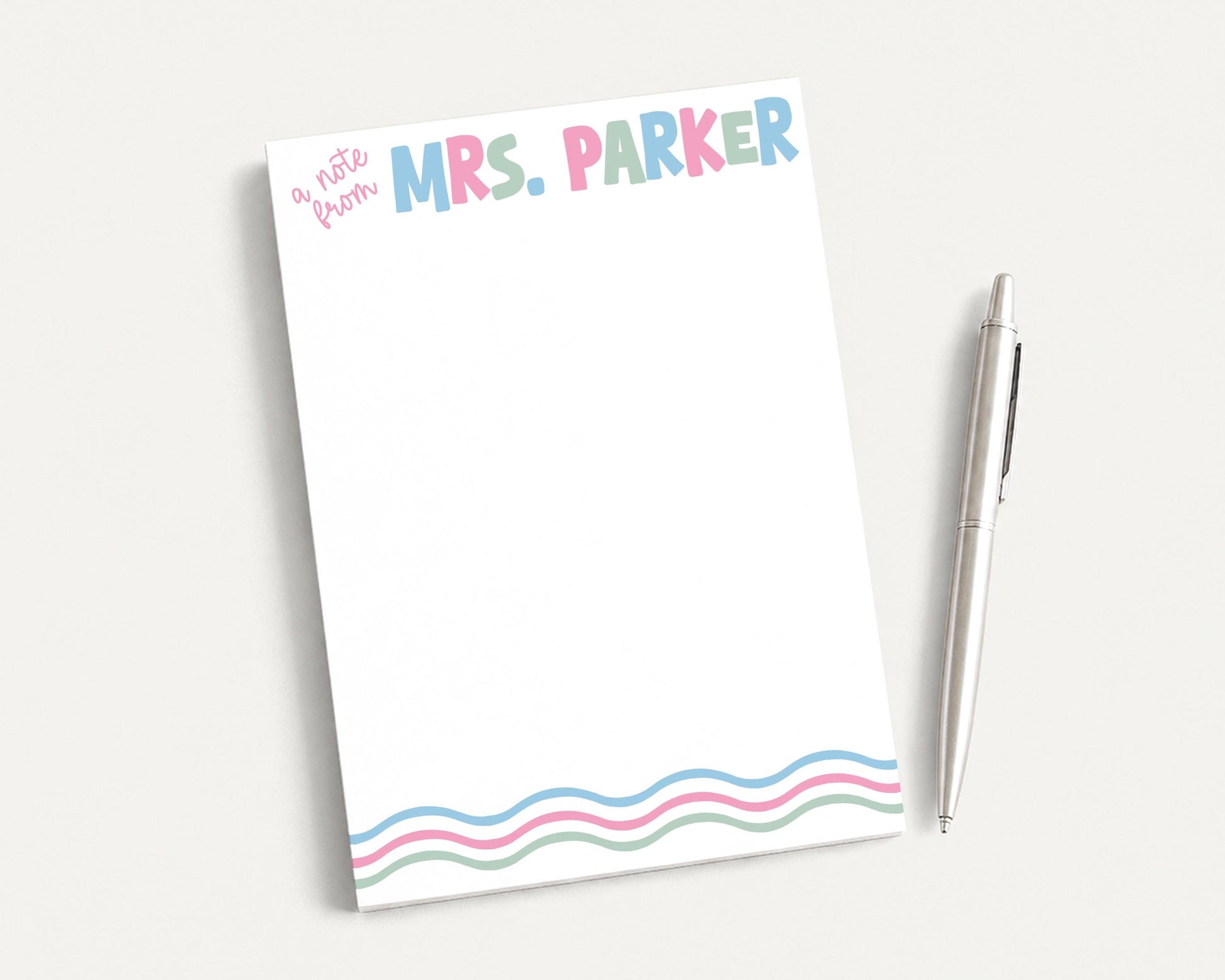 A blank notepad with the name "Mrs. Parker" written on it, along with a pen, is placed on a white surface.