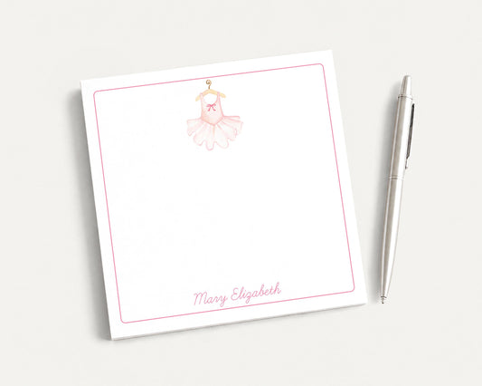 A white notepad with a pink ballet tutu illustration and the name "Mary Elizabeth" written on it, along with a pen on a plain white background.