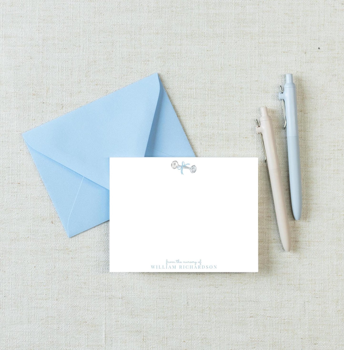 a blue envelope, a blank white card, and three pens arranged on a light-colored surface.