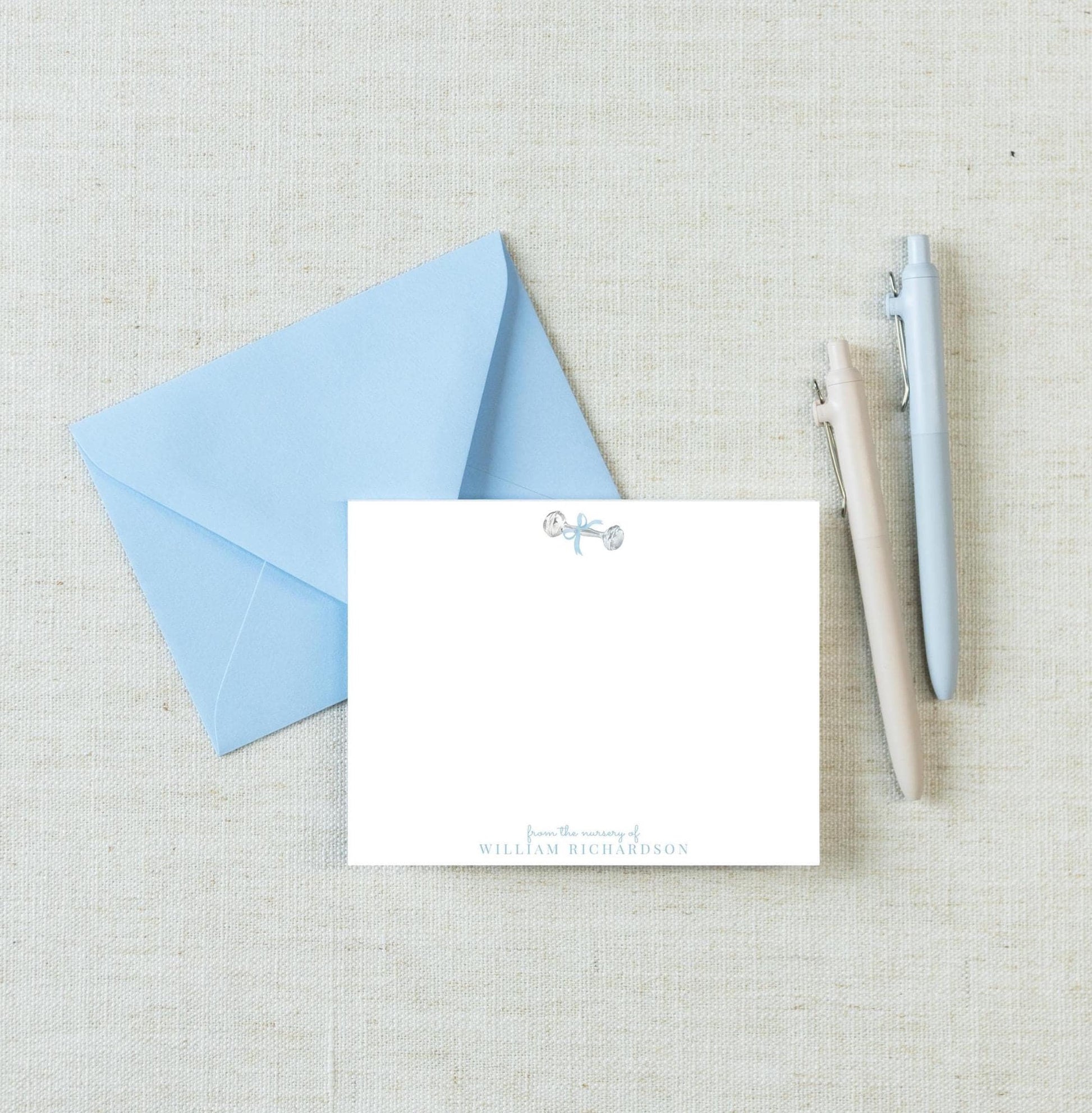 a blue envelope, a blank white card, and three pens arranged on a light-colored surface.