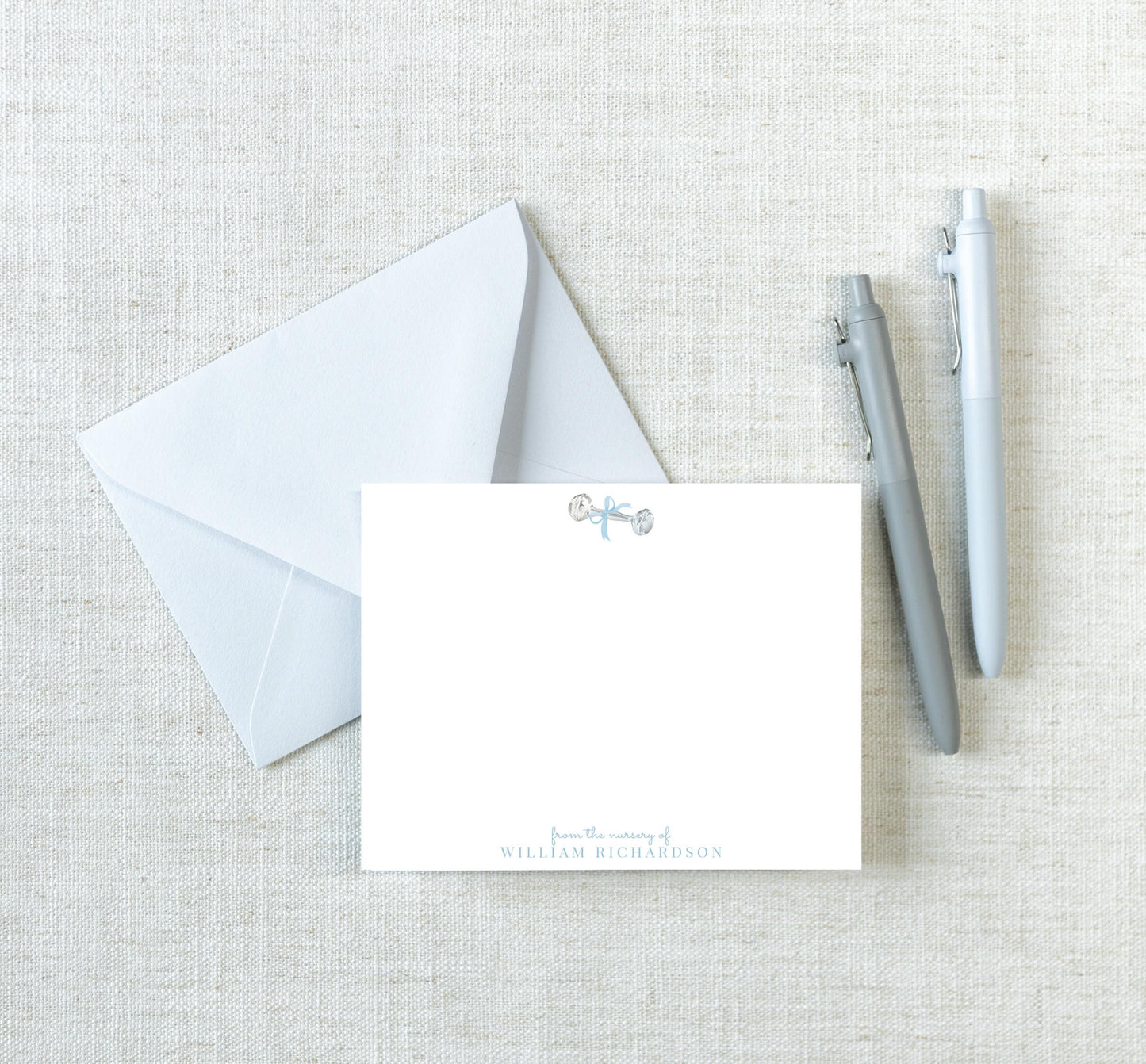a white envelope with a blank card inside, along with two pens, all placed on a beige background.