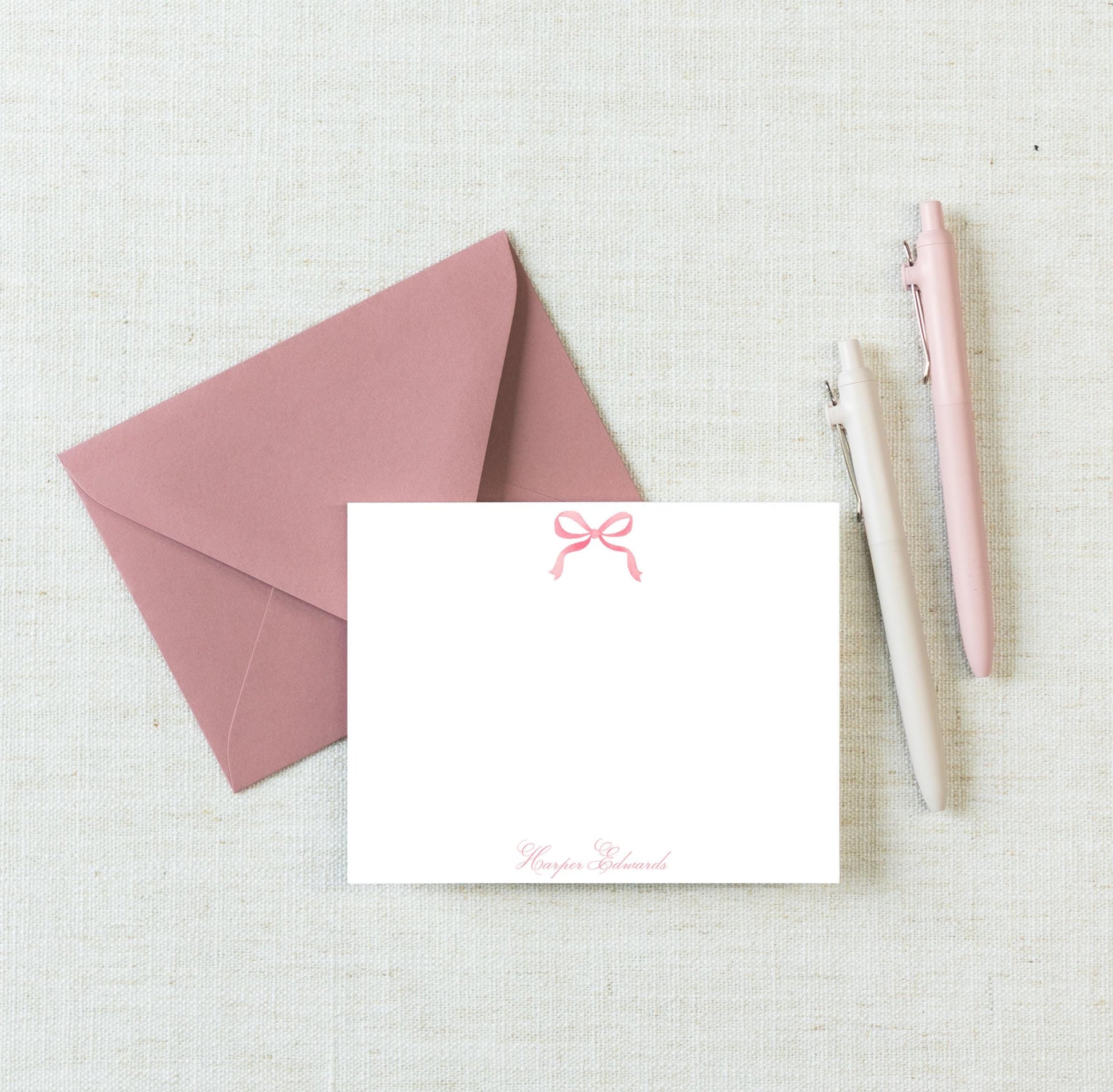 a pink envelope with a blank note card and two pens on a light-colored surface.