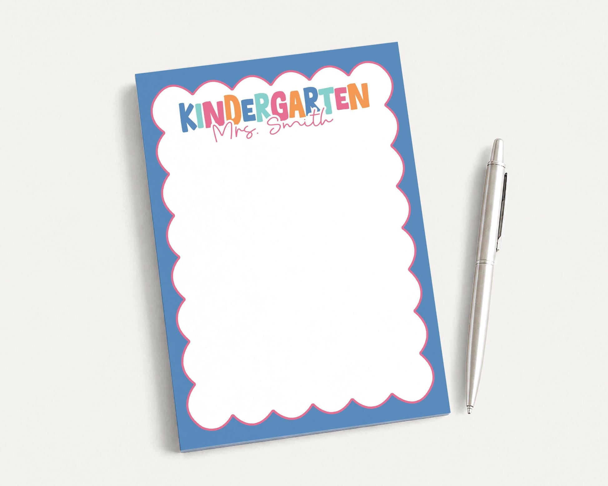 A blue notepad with a scalloped edge and a pen are placed on a white surface.