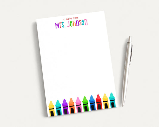 A blank white notepad with a colorful crayon design and a pen on a white surface.