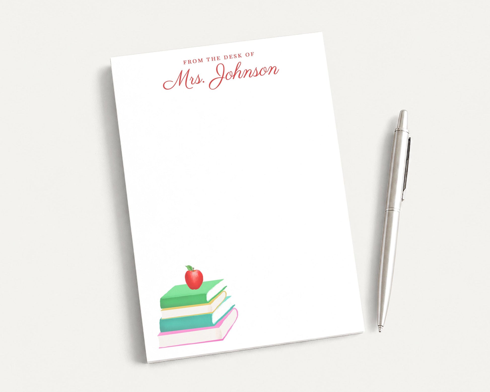 a white notepad with a stack of colorful books on top, along with a pen and a silver pen holder.