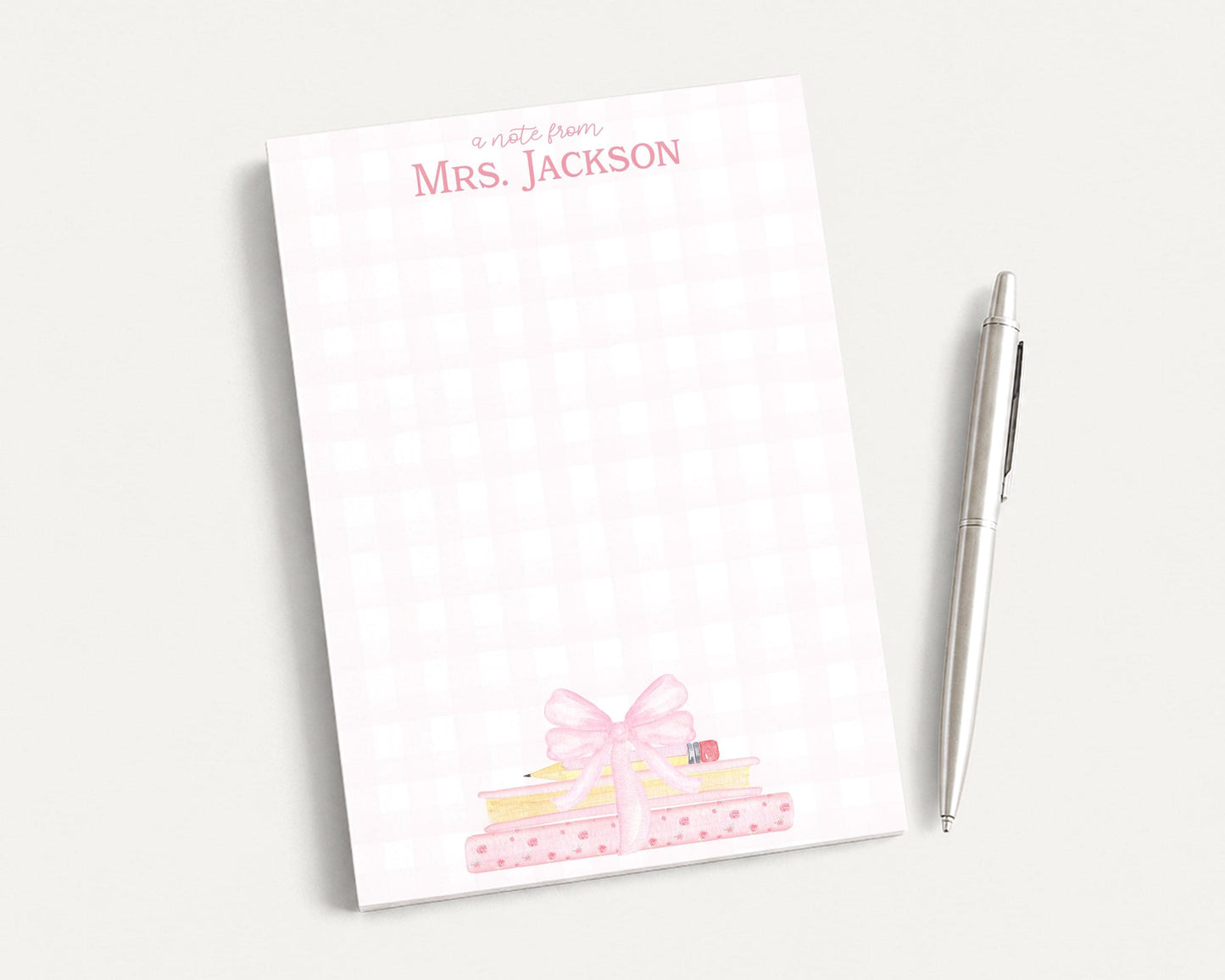 A white notepad with a pink bow and a pen on a white surface.