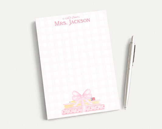 A white notepad with a pink bow and a pen on a white surface.