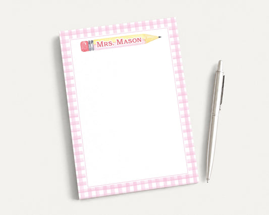 A pink and white checkered notepad with a blank page and a pen on a white surface.