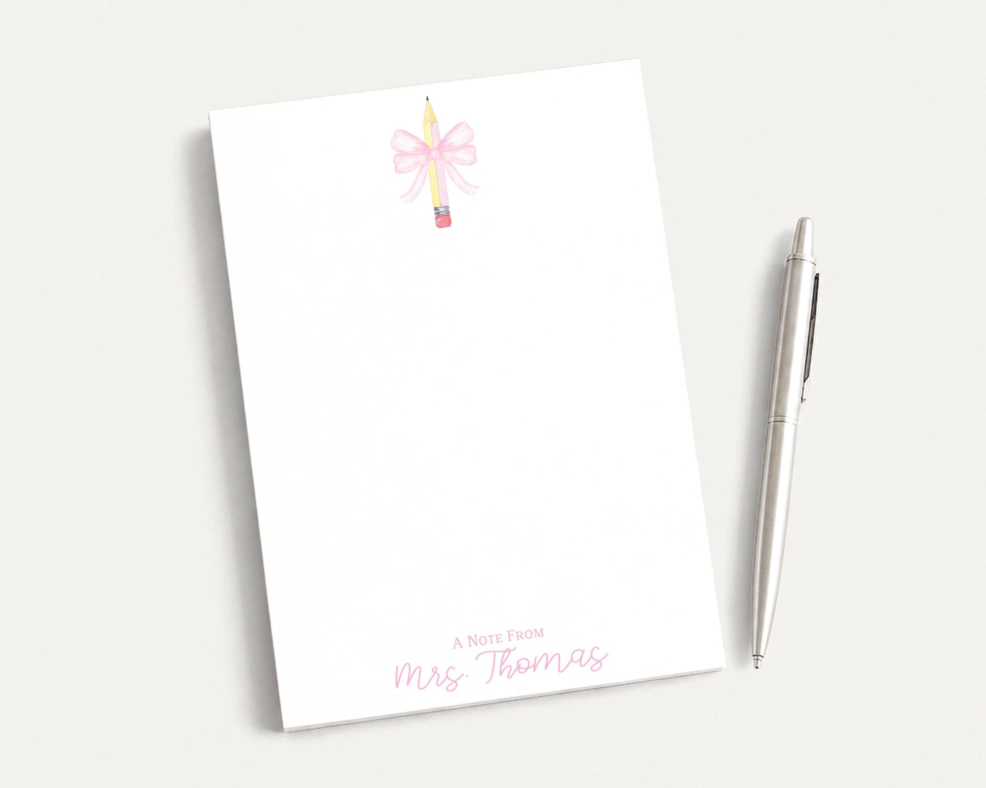 A blank white notepad with a pink bow and a pen on a white surface.